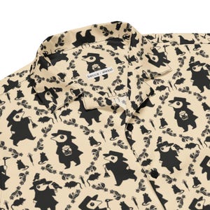 May include: A beige button-down shirt featuring a repeating black graphic pattern of plague doctors, rats, syringes, and small birds. The collar is open-style, and the interior neck label displays the text becca alessi in black lettering.
