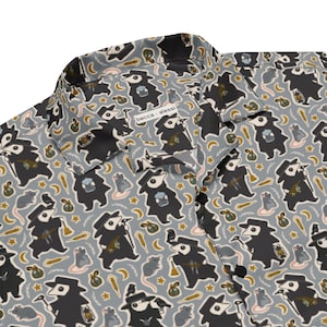 May include: Button-down shirt with a repeating pattern of plague doctor figures, rats, stars, and other small illustrations in black, gray, and tan on a light gray background. The shirt has a collar and black buttons. The text "becca alessi" is visible on the shirt.