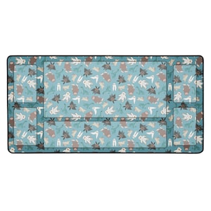May include: A rectangular desk mat with a teal background and a repeating pattern of cartoon monsters in various colors. The mat has a black border and several built-in sections for organizing items.