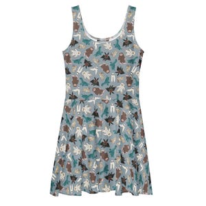 May include: A light blue skater dress featuring a repeating pattern of various cartoon monsters, including bats, ghosts, and yetis. The sleeveless dress has a scoop neckline and a flared skirt, perfect for casual wear.