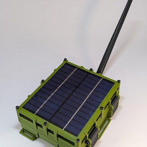 Peut inclure: Un appareil à panneau solaire vert avec une antenne noire. L'appareil a une forme rectangulaire avec une surface de panneau solaire bleu foncé. Le cadre est vert olive avec des vis et des charnières noires. L'antenne est noire et s'étend vers le haut.
