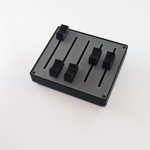 以下が含まれることがあります： 黒いプラスチック製の箱に、銀色のスライダーと黒いノブが6つ付いています。この箱は、コンピューターやその他の電子機器の制御盤として使用するために設計されています。