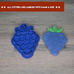 Könnte beinhalten: Zwei blaue Plastik-Ausstecher in Form von Weintrauben. Die Ausstecher liegen auf einer Holzoberfläche. Der Text "ALL CUTTERS ARE LABELED WITH NAME & SIZE" ist oben im Bild sichtbar.