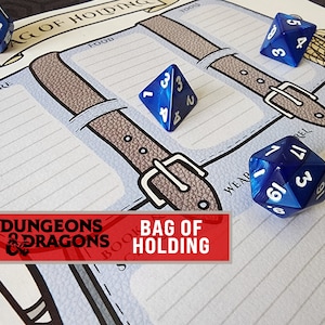 May include: A gaming mat with a "Bag of Holding" design, featuring grey straps and white lined sections. Several blue polyhedral dice are scattered around the mat. The "Dungeons & Dragons" logo is in the lower left, with the text "Bag of Holding".