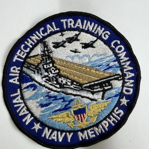 Pode incluir: Um emblema bordado circular com uma borda azul e o texto NAVAL AIR TECHNICAL TRAINING COMMAND NAVY MEMPHIS. O centro retrata um porta-aviões sobre água azul com três aeronaves pretas voando acima e um emblema de âncora dourada.