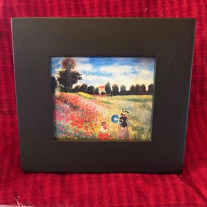 May include: A framed painting of a woman and a child walking through a field of red poppies. The painting is set against a blue sky with white clouds. The woman is holding a blue umbrella and the child is wearing a yellow hat.