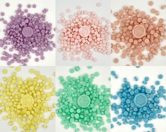 May include: Assortment of six colors of wax melts, each color is in a pile with a snowflake-shaped wax melt in the center. The colors are lavender, pink, yellow, green, and blue.