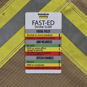 May include: A white rectangular FAST-ED Stroke Scale reference card with black text and color-coded sections in gray, yellow, red, and green. The card lists clinical criteria for facial palsy, arm weakness, and speech changes with numerical scores.