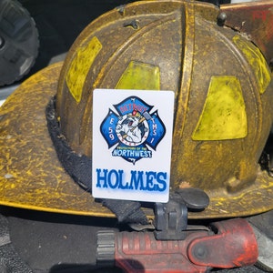 May include: A white card with a blue and red logo that says "Detroit Fire Chief" with a polar bear holding an axe. The logo is surrounded by a red star and the text "E 59 TMS 1". Below the logo is the text "Protectors of the Northwest" and the name "Holmes".
