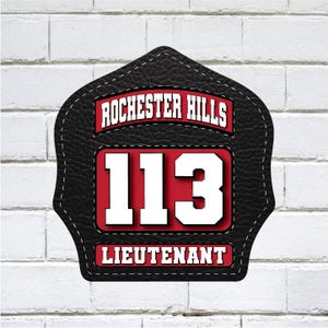 May include: A black leather-textured firefighter helmet shield with white stitching. The shield features the text "ROCHESTER HILLS" in red and white, the number "113" in white, and the word "LIEUTENANT" in red and white.