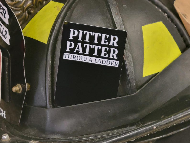 May include: A black and white card with the text "Pitter Patter Throw a Ladder" on a black background. The card is attached to a black helmet with yellow accents.