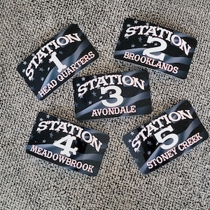 May include: Five black and white stickers with the word "Station" and a number from 1 to 5. Each sticker has a different location name below the number. The stickers have a black background with white stars and a red, white, and blue American flag design.