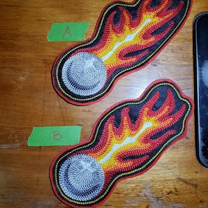 May include: Two embroidered patches shaped like a comet or fireball. Each patch features a gray sphere, a white and yellow streak, and red and black flames. The patches are outlined in black and red.