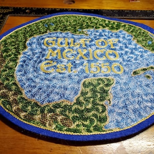 May include: Embroidered patch featuring the Gulf of Mexico, with blue water and green landmasses. Gold text reads "GULF OF MEXICO Est. 1550" on a blue felt background. The patch has a gold border and is circular in shape.