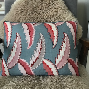 May include: A blue cushion with a pattern of pink and red stylised leaves. The cushion is sitting on a fluffy, light brown sheepskin.
