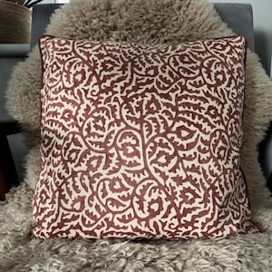 May include: A red and white patterned cushion with a floral design. The cushion is sitting on a fluffy white sheepskin rug.