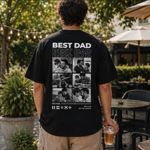 Puede incluir: Camiseta negra con la frase "BEST DAD" apilada tres veces en blanco. Debajo del texto hay seis fotos en blanco y negro. La camiseta tambi&eacute;n tiene el nombre "MICHAEL" y la frase "BEST DAD IN THE WORLD!" impresos.