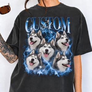 May include: A charcoal gray t-shirt featuring a graphic print of five Siberian Husky dog faces arranged in a cluster. The design includes blue lightning bolts, sparkling star accents, and the text "CUSTOM Text" in a bold blue font.