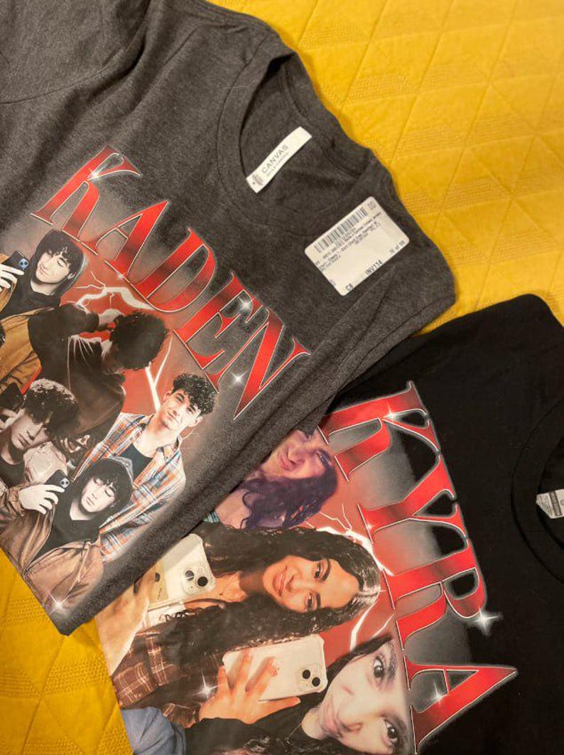 Puede incluir: Se muestran dos camisetas, una gris antracita y otra negra. La camiseta gris presenta un gr&aacute;fico con el nombre "KADEN" en texto rojo estilizado y un collage de personas. La camiseta negra tiene un dise&ntilde;o similar.