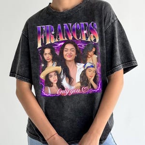 May include: Dark gray t-shirt featuring a graphic of a woman with the name "FRANCES" in a purple and orange font. The graphic includes multiple images of the woman and the text "Only you" with a heart symbol. The shirt has a vintage, washed appearance.