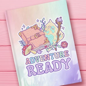 May include: A pastel rainbow notebook with a whimsical illustration of a closed book, a map, a wand, a mushroom, and a dice. The text "Adventure Ready" is written in a colorful, retro font.