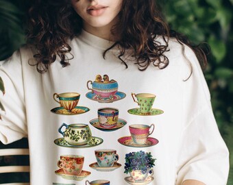 Puede incluir: Una camiseta blanca con un patrón colorido de tazas de té y platillos. El texto "IVORY" está escrito en forma de nube en la esquina inferior derecha de la imagen.