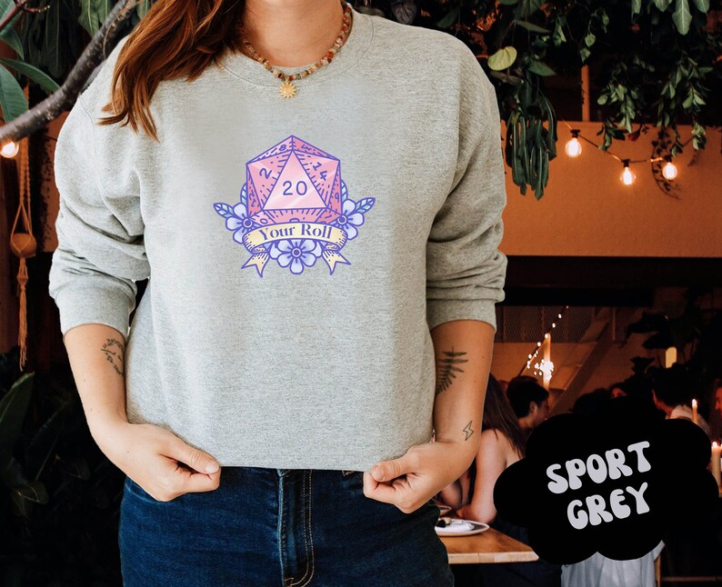 May include: A grey sweatshirt with a pink and blue graphic of a twenty-sided die with the text "Your Roll".