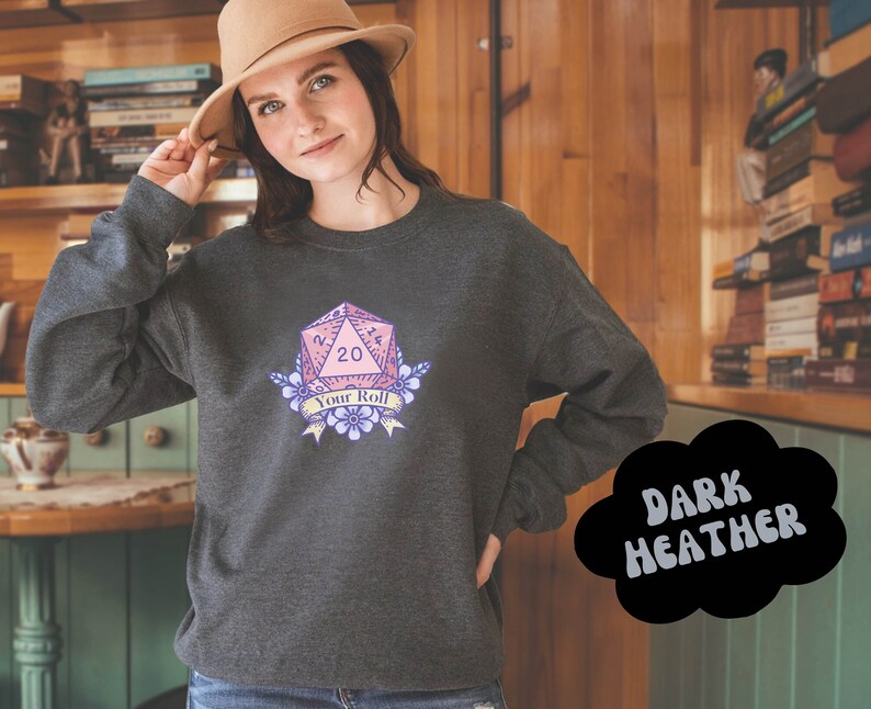 May include: Dark heather grey sweatshirt with a pink and purple 20-sided die graphic with the text "Your Roll".