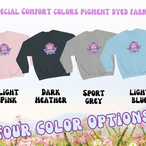 May include: Four colour options for a sweatshirt featuring a pink 20-sided die with the text "You Roll Girl" and floral accents. The sweatshirt colours are light pink, dark heather, sport grey, and light blue.
