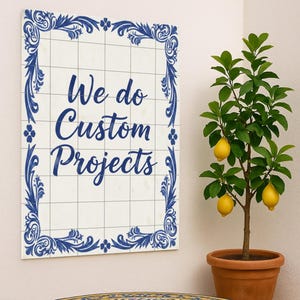 May include: A round outdoor table with a tiled top featuring a blue and yellow floral pattern. A sign with the text "We do Custom Projects" hangs above. A potted lemon tree with ripe lemons is to the right.