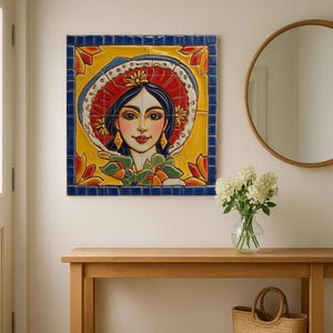 Könnte beinhalten: Ein farbenfrohes Keramikfliesenkunstwerk mit einer Frau mit dunklem Haar und einem roten Hut. Das Kunstwerk ist mit einem blauen Rahmen versehen und an einer weißen Wand angebracht. Eine Holzkonsolentisch mit rundem Spiegel und einem Weidenkorb befinden sich im Vordergrund.