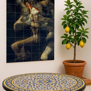 Puede incluir: Mesa redonda con una encimera de azulejos decorativos con un patrón floral azul y amarillo. La mesa tiene una estructura de metal negro. Un limonero en maceta con limones maduros está cerca, y una obra de arte enmarcada cuelga de la pared.
