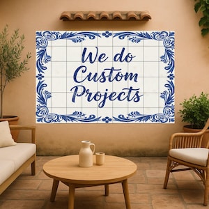 以下が含まれることがあります： 青いスクリプトで「We do Custom Projects」と書かれた装飾的なタイルパネル。パネルは青い花の模様で縁取られています。シーンには、ソファ、丸い木製のテーブル、籐の椅子が含まれています。
