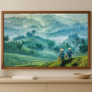 May include: A framed print of a tea plantation landscape, featuring rolling green hills and misty blue mountains. Two figures in traditional dress walk along a path, carrying baskets. The artwork is displayed on a neutral-toned cabinet.