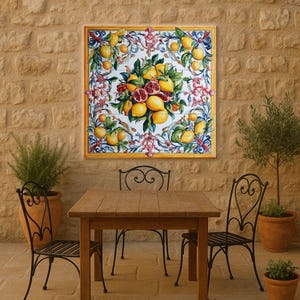 以下が含まれることがあります： レモンとザクロの鮮やかな静物画を描いた、正方形の額入りタイルアート。装飾的な花の要素を配した白い背景に作品が配置されています。フレームは黄色で、作品は質感のある石壁に取り付けられています。