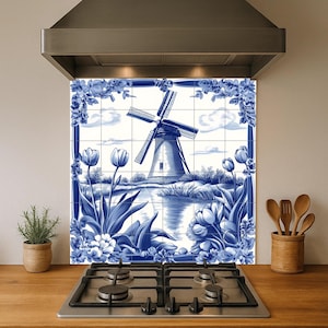 May include: Blue and white tile backsplash featuring a Dutch windmill scene with tulips and floral border. The artwork is installed above a gas stove and is framed by a stainless steel range hood. The kitchen decor includes a small potted plant and wooden utensils.