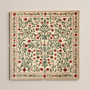 May include: A square, off-white textile with a floral design. The pattern features red flowers and green leaves arranged in a symmetrical tree-like pattern. A red border frames the design, adding a decorative touch.