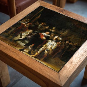 Könnte beinhalten: Quadratischer Beistelltisch aus Holz mit einer gefliesten Oberseite, die eine Reproduktion von Rembrandts "Die Nachtwache" zeigt. Der Tisch hat eine natürliche Holzoberfläche und misst ca. 50 cm im Quadrat und 46 cm hoch.