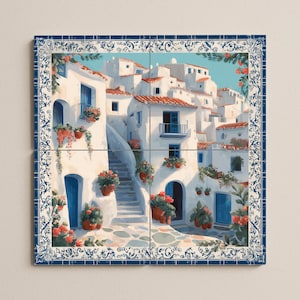 Op de afbeelding: Een aquarel schilderij van een mediterrane dorpsscène. Witte gebouwen met rode pannendaken en blauwe deuren en luiken tegen een blauwe lucht. Het kunstwerk is omlijst door een blauw-witte decoratieve rand.