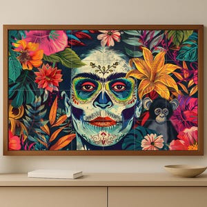 Könnte beinhalten: Gerahmter Kunstdruck mit einer farbenfrohen Illustration eines Gesichts mit Zuckerschädel-Make-up, umgeben von leuchtenden Blumen und Blättern. Ein kleiner Affe ist ebenfalls im Kunstwerk vorhanden. Die Farbpalette umfasst Blau-, Orange- und Rosatöne.