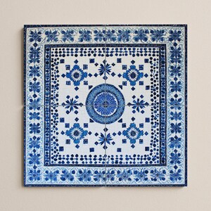 Può includere: Piastrella decorativa quadrata con un motivo floreale blu e bianco. La piastrella presenta un design circolare centrale circondato da fiori stilizzati e forme geometriche. Il bordo è adornato da un motivo floreale ripetuto.