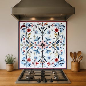 May include: A decorative kitchen backsplash featuring a floral design in red, blue, and pink hues. The backsplash is composed of square tiles and is installed above a gas stovetop. A stainless steel range hood is mounted above the backsplash.