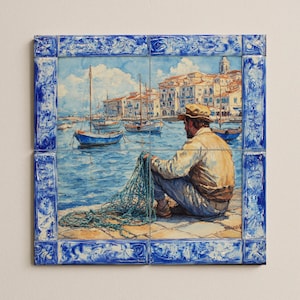 May include: A ceramic tile artwork depicting a seaside scene. A man sits on a stone pier, holding a fishing net, with boats and buildings in the background. The artwork is framed with a blue and white decorative border.