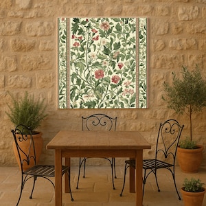 May include: A framed floral print featuring a repeating pattern of red and pink flowers, green leaves, and vines on a cream background. The print is displayed above a wooden table and wrought iron chairs on a stone patio.
