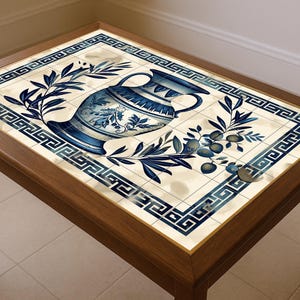 Puede incluir: Mesa de centro rectangular de madera con tapa de azulejos. El azulejo presenta un borde de llave griega azul y blanco y un diseño central de un jarrón con ramas de olivo. La mesa tiene cuatro patas en ángulo.