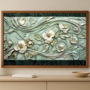 Op de afbeelding: Een ingelijste bloemenreliëfsculptuur. Het kunstwerk toont witte bloemen, groene bladeren en wervelende ranken tegen een lichtblauwe achtergrond. De lijst is van donkerbruin hout. Het kunstwerk wordt tentoongesteld op een lichtbeige kast.