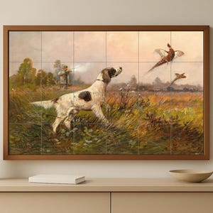 Può includere: Un'opera d'arte incorniciata raffigurante una scena di caccia con un cane, un cacciatore e uccelli in volo. Il cane, con macchie nere, è in primo piano, con il cacciatore sullo sfondo. L'opera è in una cornice di legno.