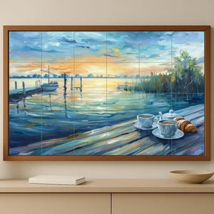 May include: A framed landscape painting depicting a serene waterscape at dawn or dusk. The artwork features a pier, boat, and cups of coffee with a croissant on a wooden surface. The color palette includes blues, oranges, and greens.