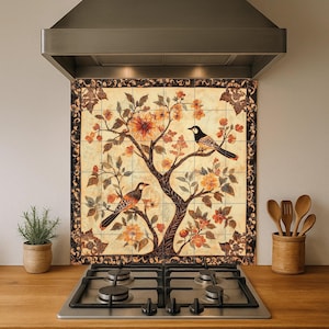 Puede incluir: Salpicadero de cocina decorativo con un árbol con flores naranjas y dos pájaros. El diseño está enmarcado con un borde oscuro. El salpicadero está instalado encima de una cocina de gas y debajo de una campana extractora de acero inoxidable.