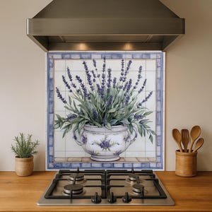 Puede incluir: Un protector de cocina con un diseño floral de lavanda en una maceta decorativa blanca y azul. El protector está rodeado de azulejos azules. Una campana extractora de acero inoxidable está encima. Una placa de gas está al frente.
